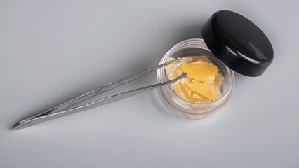 high thc cannabis concentrate,tweezers and container with piece wax extract on gray background.