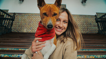 Happy woman with authentic real smile looks at camera and hug, hold on lap adorable cute puppy of basenji breed. Dog and woman laughing and enjoying life
