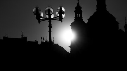 Obraz premium Black and white Prague City buildings silhouette with church with white sun in sunset in the middle 