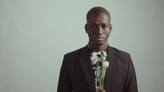 Studio portrait of young adult African American man wearing black jacket with floral pattern shirt holding small flower bouquet looking at camera. Suitable for deepfake generation or face swap
