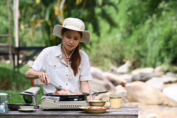 Young female traveler grilled bbq near the river bank surrounded by beautiful nature. Adventure, travel, tourism and camping concept