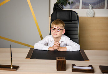 serious boy in glasses sitting in the director's chair in the office of the school
