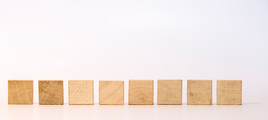 Acht quadratische Holzsteinen in einer Reihe vor weißem Hintergrund als Vorlage oder Mockup. Leere Scrabblesteine.