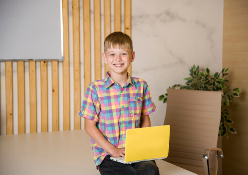 Smiling Happy Boy Sitting At The Table In Classrroom With Yellow Laptop