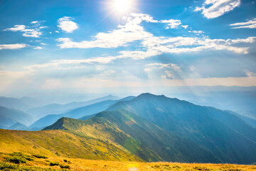 Mountains landscape with peaks, sun, clouds and grass field