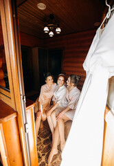 Pretty bride with bridesmaids in dressing gowns sitting on the bed cute hug each other.