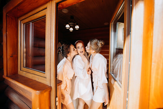 Beautiful bride with bridesmaids in bathrobes posing in a room in a wooden style.