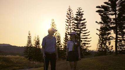 Couple Golfing player talking about nice shot in golf course after hit the golf ball to hole for score, sports relax in holidays summer vacation at sunset golden time, cinematic