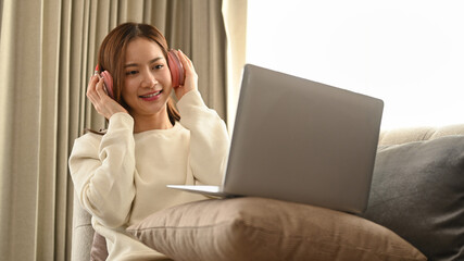 Smiling young woman with headphone using laptop, spending leisure time on a bright autumn morning