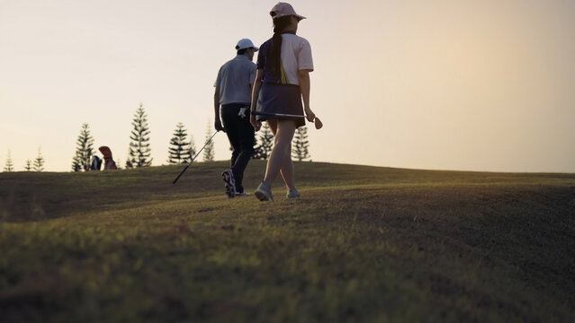 Couple Golfing player talking about nice shot in golf course after hit the golf ball to hole for score, sports relax in holidays summer vacation at sunset golden time