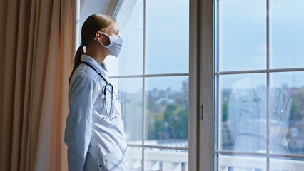 Beautiful young woman doctor with a protective mask she take a break looking through the panoramic window and thinking