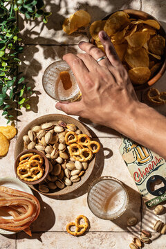 Beer Outdoor Party Concept. Man's Hand Takes A Glass Of Beer From The Table With Different Snacks. Still Life On Tile Background With Hard Shadows, Top View