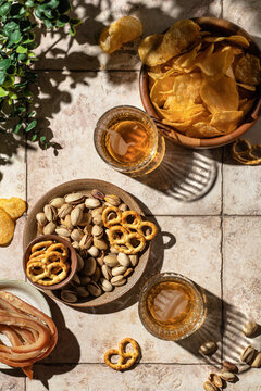 Summer beer outdoor party concept. Two glasses of beer with different snacks, chips, nuts, pretzels on tile background with hard shadows, top view