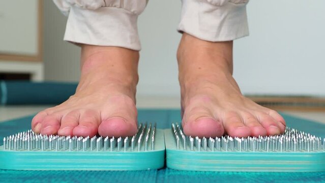 Deep relaxation standing barefoot on a bed of nails. A woman practices sadhu yoga. Close-up front view of bare feet and a sadhu wooden board. Camera movement removal.