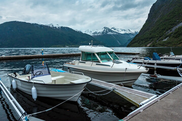 Fototapeta na wymiar Motorboats, yachts, sailing and fishing boats moored to a pier in a small village in fjords.