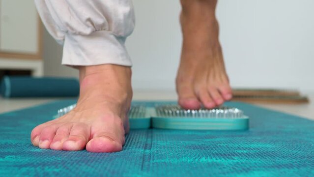 Sadhu wooden blue board with nails, female feet stepping on sharp nails for meditation, leg relaxation, acupuncture tool. Exercises for relaxation and harmonization of the soul, sadhu yoga practice.