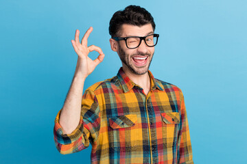 Photo of flirty handsome cheerful guy in eyeglasses dressed checked shirt showing okey sign winking...