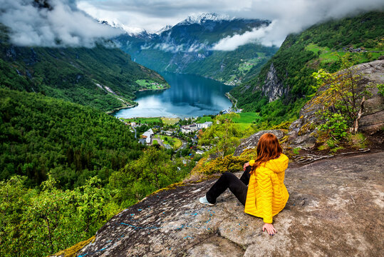 Woman in yellow sitting on the rock above Geiranger