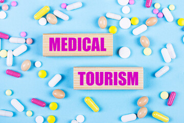 On a light blue background, multi-colored pills and wooden blocks with the text MEDICAL TOURISM. Pharmaceutics. Medical concept.