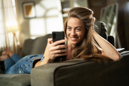 Happy young woman using the phone at home. Excited woman enjoying in the living room.