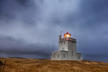 Fototapeta na wymiar Dyrholaey Lighthouse at blue hour in autumn, the most southerly point on mainland Iceland. Storm clouds are rolling in around the mountains behind