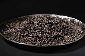 Black tea loose dried tea leaves in a black stone plate, marco