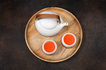 A white teapot and two cups of lemongrass tea on a wooden tray. View from above.