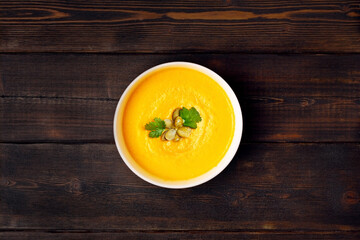 Pumpkin soup in a bowl, sprinkled with pumpkin seeds on dark wooden background, top view.