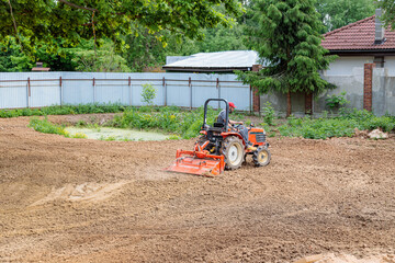 A man on a mini-excavator levels a piece of land, loosens the soil.