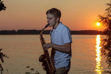 A young guy plays the saxophone in the evening at sunset