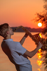 A young guy plays the saxophone in the evening at sunset