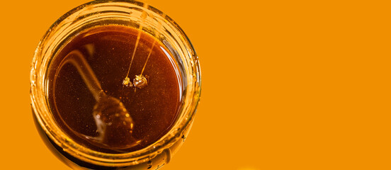 Glass jar with natural honey on orange background, two jets of flower honey flow down into the jar,...