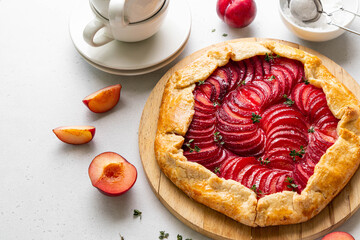 Plum galette with thyme on wooden board on light background. Healthy homemade fruit pie with plums....