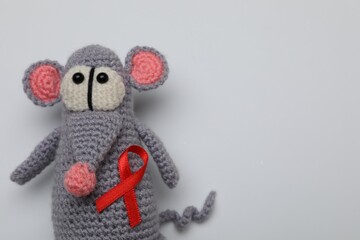 Cute knitted toy mouse with red ribbon on light grey background, top view and space for text. AIDS disease awareness
