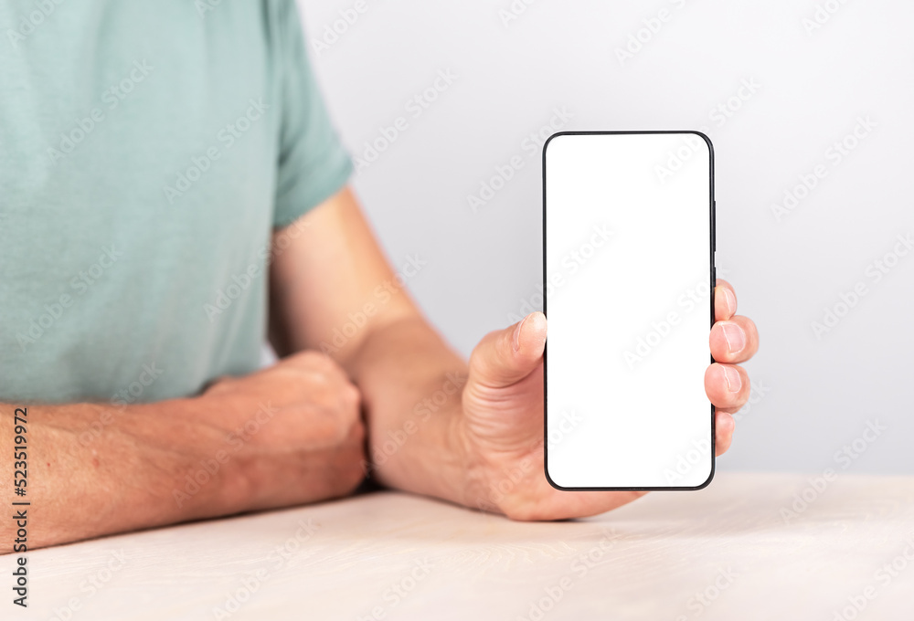 Poster Man holding phone mockup in vertical position. Android with empty screen for advertising. Male sitting at table and showing smth at smartphone. High quality photo
