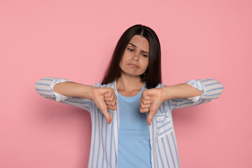 Young woman showing thumbs down on pink background