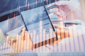 Double exposure of man's hands holding and using a phone and financial chart drawing. Market...