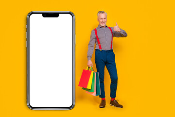 Full length body size view of handsome trendy cheerful man buying bags showing thumbup isolated over bright yellow color background