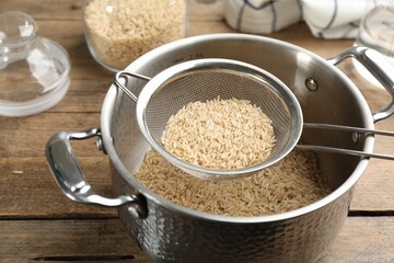 Sieve with rice in pot on wooden table, closeup