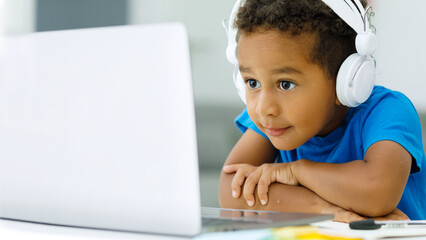 Little african american boy homeschooled studying with headphones during virtual internet class online with school teacher
