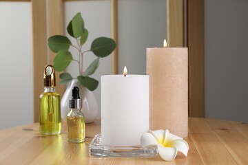 Burning candles, essential oil and plumeria flower on wooden table