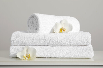 Clean soft white towels with flowers on table against light grey background