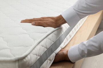 Man touching soft white mattress indoors, closeup