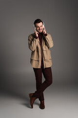 Full length of stylish man in autumn outfit and headphones standing on grey background.
