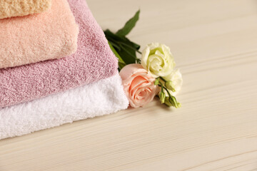 Obraz na płótnie Canvas Soft folded towels, rose and eustoma flowers on light wooden table, closeup