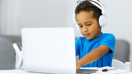 Cute little african american boy studying with laptop with headphones remotely at home enjoying distance learning - Powered by Adobe