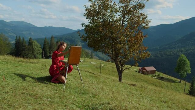 Inspired girl creating picture on green hill. Woman painting sketch on easel.