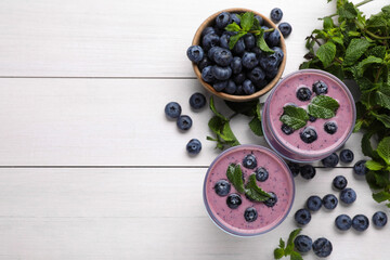 Naklejka na ściany i meble Glasses of blueberry smoothie with mint and fresh berries on white wooden table, flat lay. Space for text