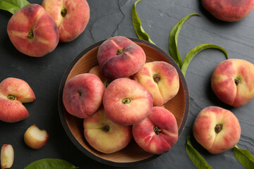 Fresh ripe donut peaches with leaves on dark table, flat lay