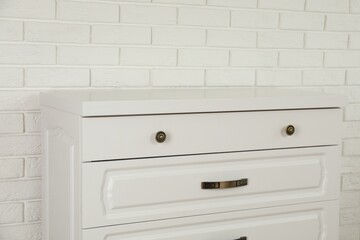 Modern chest of drawers near white brick wall